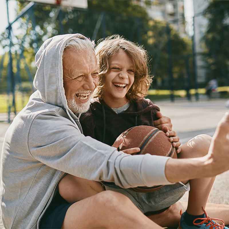 Grandfather and grandson laughing on the basketball court.